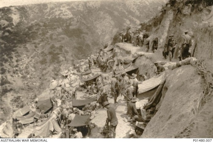 GALLIPOLI. 1915. STEELE'S POST, SHOWING DUGOUTS, HELD BY MEMBERS OF THE 8TH INFANTRY BATTALION, WITH MEN WALKING ALONG THE NARROW PATH CUT INTO THE STEEP HILLSIDE ABOVE.